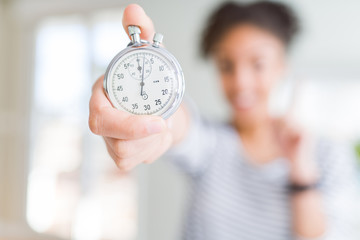 Young african american woman holding stopwatch surprised with an idea or question pointing finger with happy face, number one