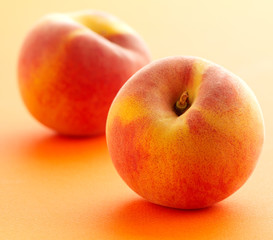 2 whole peaches, 1 in focus on peach coloured background