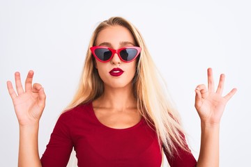 Young beautiful woman wearing red t-shirt and sunglasses over isolated white background relax and smiling with eyes closed doing meditation gesture with fingers. Yoga concept.