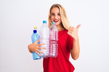 Young beautiful woman recycling plastic bottles standing over isolated white background happy with big smile doing ok sign, thumb up with fingers, excellent sign