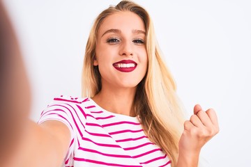 Beautiful woman wearing striped t-shirt make selfie by camera over isolated white background screaming proud and celebrating victory and success very excited, cheering emotion