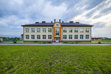 New modern two-storied kindergarten preschool building with big windows on green grassy lawn and blue sky copy space background. Architecture and development concept.