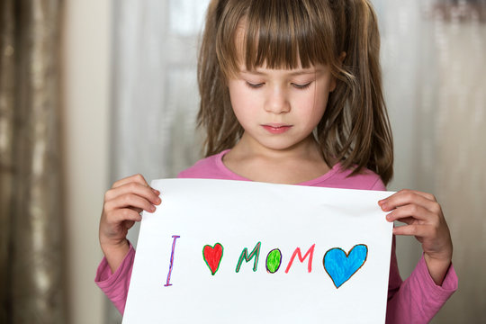 Cute child girl wit sheet of paper with colorful crayons painted words I love Mom. Art education, creativity concept.