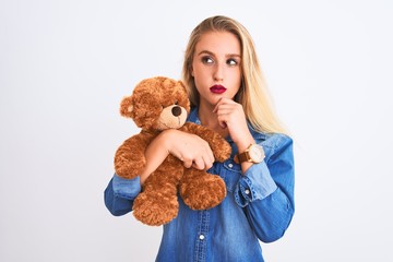 Young beautiful woman holding cute teddy bear standing over isolated white background serious face thinking about question, very confused idea