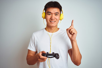 Young asian chinese gamer man playing video game standing over isolated white background surprised with an idea or question pointing finger with happy face, number one © Krakenimages.com