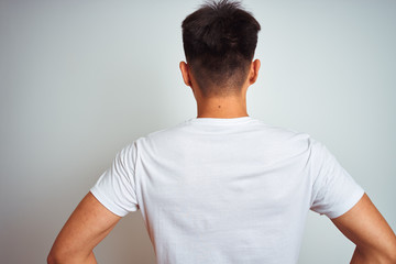 Young asian chinese man wearing t-shirt standing over isolated white background standing backwards...
