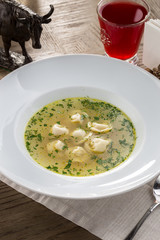 Bouillon with meat dumplings on white plate and red drink on wooden table