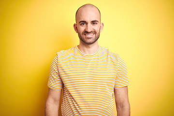 Fototapeta premium Young bald man with beard wearing casual striped t-shirt over yellow isolated background with a happy and cool smile on face. Lucky person.