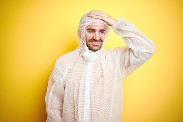 Young man wearing painter equipment and safety glasses over isolated yellow background stressed with hand on head, shocked with shame and surprise face, angry and frustrated. Fear and upset