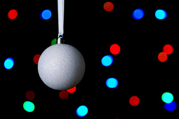 White Christmas ball on a black background with colored lights.