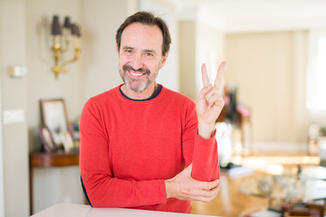 Handsome middle age man at home smiling with happy face winking at the camera doing victory sign. Number two.