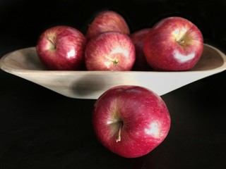 una manzana en primer plano y detrás manzanas en una fuente de madera rustica, sobre fondo negro