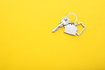 House keys with trinket on color background, top view with copy space.