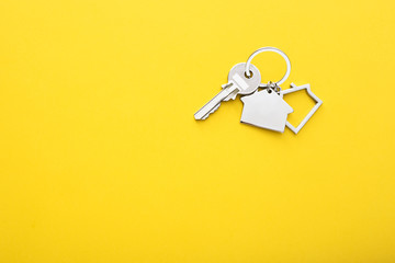 House keys with trinket on color background, top view with copy space.