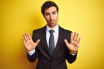 Young handsome businessman wearing suit and tie standing over isolated yellow background Moving away hands palms showing refusal and denial with afraid and disgusting expression. Stop and forbidden.