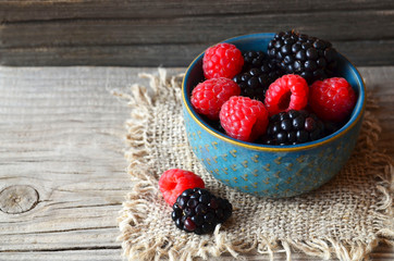 Fresh ripe organic blackberries and raspberries in a blue bowl on rustic wooden table.Summer berries.Healthy eating,vegan food or diet concept. Selective focus.
