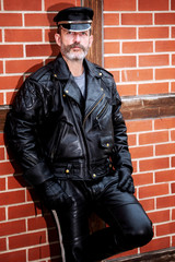 handsome sexy bearded man dressed in black leather leaning against brick wall