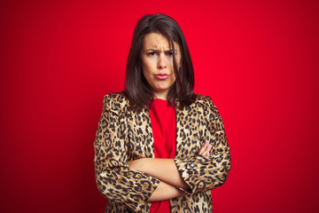 Young beautiful brunette woman wearing a leopard jacket over red isolated background skeptic and nervous, disapproving expression on face with crossed arms. Negative person.