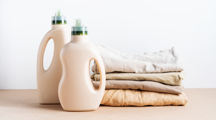 Stack of folded clean clothes things with Eco Design mockup blank bottles packaging of detergent for laundry on white background. Space for text. Bio organic product.