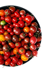 Multi-colored motley cherry tomatoes on a black plate, white background. Cropped image