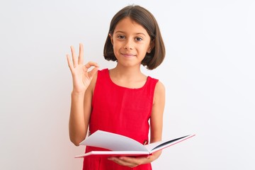 Beautiful student child girl reading red book standing over isolated white background doing ok sign with fingers, excellent symbol
