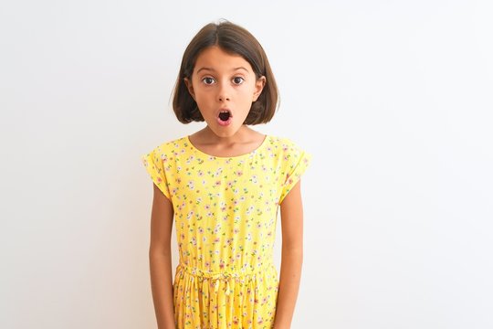 Young beautiful child girl wearing yellow floral dress standing over isolated white background afraid and shocked with surprise and amazed expression, fear and excited face.