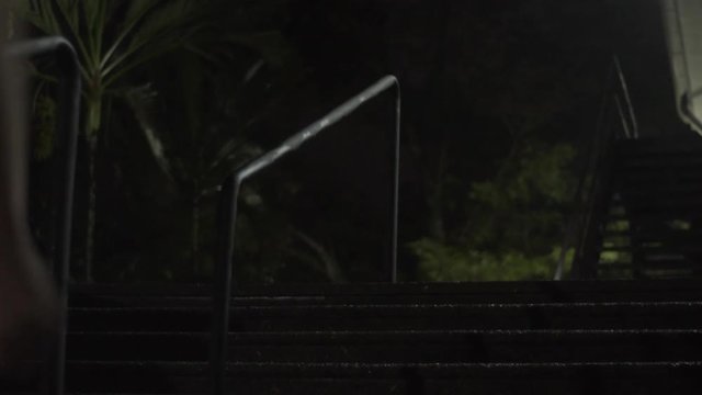 Joven apresurado corriendo de noche bajando escaleras h&uacute;medas