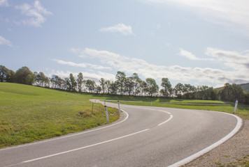 Kurvige Straße mit Baumreihe und Wolkenhimmel