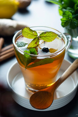 Glass cup of ginger tea with lemons and mint leaves on dark background. Ginger tea, drink ingredients, cold and autumn time.