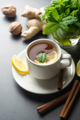 Cup of ginger tea with lemons and mint leaves on dark background. Ginger tea, drink ingredients, cold and autumn time.