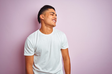 Young brazilian man wearing t-shirt standing over isolated pink background looking away to side with smile on face, natural expression. Laughing confident.