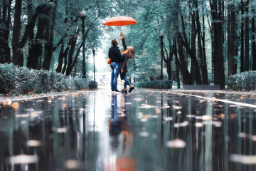 rain in the autumn park / young 25 years old couple man and woman walk under an umbrella in wet rainy weather, walk October lovers - obrazy, fototapety, plakaty