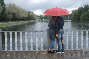 Obraz premium rain in the autumn park / young 25 years old couple man and woman walk under an umbrella in wet rainy weather, walk October lovers