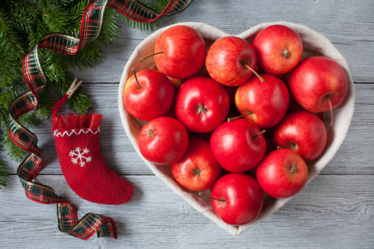 Red apples, basket in the form of heart on a wooden background, sock and branches of a fir