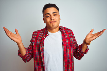 Young brazilian man wearing red shirt standing over isolated white background clueless and confused...