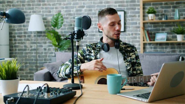 Blogger handsome young man is playing the guitar and singing recording music in modern studio using microphone, laptop and sound mixer. People and blogging concept.