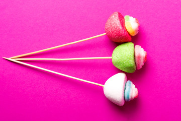 marshmallow candies on wooden sticks on a pink background, top view