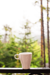 White coffee cup on the balcony with blurred nature view and forest background, after rain