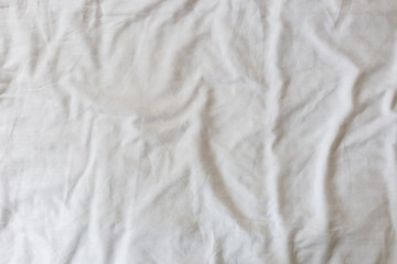 Fototapeta na wymiar Abstract pattern of a white crumpled bed sheet in a hotel room. The manufacturing of bedsheet uses cotton, linen, silk modal and bamboo rayon.