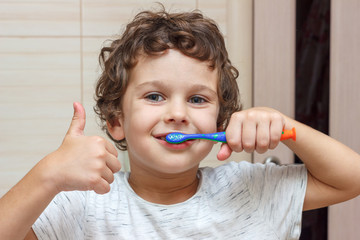 Cute little boy is brushing his teeth with toothbrush and showing thumb up. The concept of children's health, medicine.