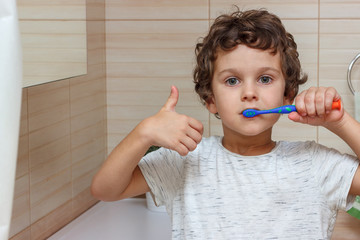 Cute little boy is brushing his teeth with toothbrush and showing thumb up. The concept of children's health, medicine.