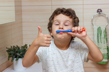 Cute little boy is brushing his teeth with toothbrush and showing thumb up. The concept of children's health, medicine.