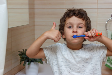 Cute little boy is brushing his teeth with toothbrush and showing thumb up. The concept of children's health, medicine.