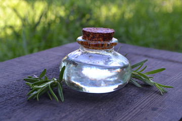 Essential oil of rosemary in little glass bottle, on rustic wooden table. Spa skin care concapt. Rosemary branch.