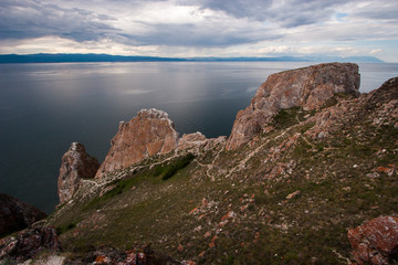 Rocks Three Brothers on the island of Olkhon on Baikal lake. Sky with clouds. On the stones is red moss. Beautiful sky, it is raining in the distance, mountains are visible.