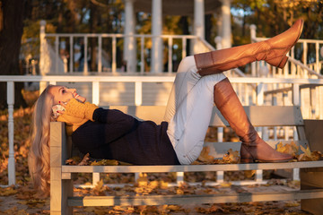 Autumn girl talking on the phone while lying on a bench in a park, after a walk