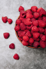 clay plate with tasty bright raspberries on a gray background