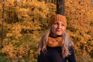 In autumn, a woman stands and looks at us not in the forest beautiful leaves, she is in a hat and...