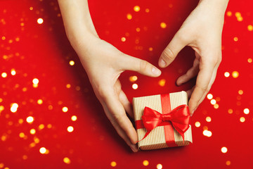 Hands holding gift in craft box on the red background. with lights. The concept of St. Valentine's day, New Year, Christmas, holidays, weddings, engagements, Mother's Day, birthday. Flat lay