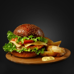 Appetizing burger with sauce and side dish on a wooden board.